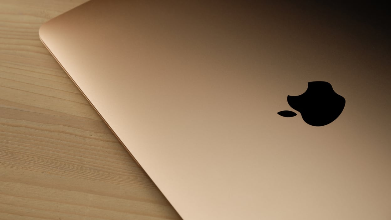 rose gold macbook air (2020) on a wooden table with the Apple logo highlighted in black, close up.