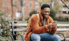 man sitting on park bench and smiling at his phone
