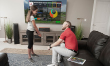 A dad sitting and watching his daughter use the TruGolf Mini Golf Simulator in front of a TV screen