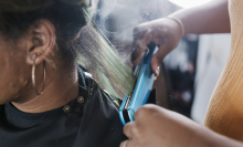 A close up of a black hairdresser straightening a client's hair with some steam rising from the heat.