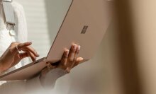 The Microsoft Surface Laptop 3 in a rose gold color held up while someone while they're standing