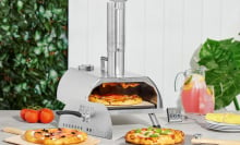 Wolfgang Puck pizza oven surrounded by pizzas, tomatoes, lemonade, and more.