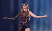 Swift in her black and red "Reputation"-era leotard on stage, arms outstretched to either side.