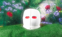 white mask with red LED light shining through eye holes against grass and flower background