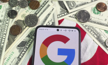 A Google logo on a phone resting on an American flag with dollar bills and coins around it. 