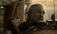 A pirate looks forlorn at the helm of a ship.