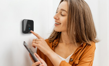 A woman touching the Cielo Smart Thermostat while smiling.