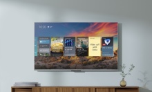 Amazon Fire TV hanging on wall with apps and sunset on screen and TV stand with decor below
