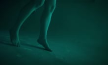 A pair of legs are visible underwater in a pool at night, lit with a dim green light.