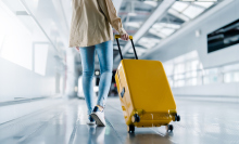 A woman in denim jeans rolling a bright yellow suitcase through an airport. 