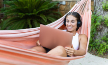 woman with headphones on using laptop in a hammock 