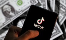 A phone displaying the TikTok logo surrounded by American cash. 
