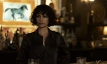 A woman in a black blouse stands behind a bar.