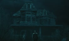 A man stands in front of a tall, dilapidated house at night.