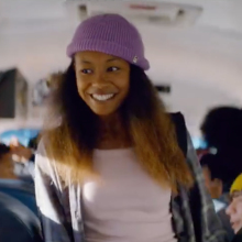 A girl standing in the aisle of a school bus smiling.