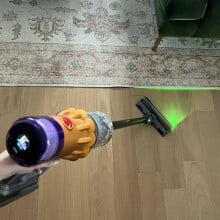 Person holding Dyson V12 Detect Slim to clean hardwood floor with laser on