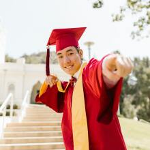 a man in red academic regalia smiling while wearing mortarboard