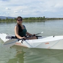 Person with long hair wearing a green top in a white oru kayak on a lake
