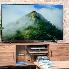 The 50-inch AU8000B Smart TV from Samsung standing on top of living room shelving surrounded by a plant and accessories