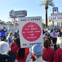 SAG-AFTRA and WGA workers gather in Las Vegas. A person holds a sign that reads, "We're not Dumbo. We won't work for peanuts."