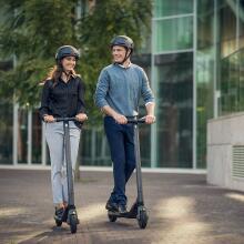 Two people riding the Segway Ninebot KickScooter ES2 with helmets on.