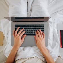 person typing on laptop in bed