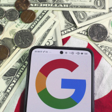 A Google logo on a phone resting on an American flag with dollar bills and coins around it. 
