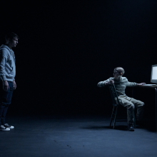 A man stares at a child sitting at a computer in "Dear David." 