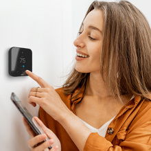 A woman touching the Cielo Smart Thermostat while smiling.