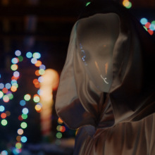 A promotional still from "It's a Wonderful Knife" showing the killer in a white mask, with Christmas lights in the background.