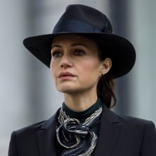 A woman stands outside wearing a wide-brim black hat.