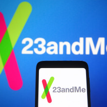 A phone displaying the The 23andMe logo in front of a larger 23andMe logo. 