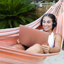 woman with headphones on using laptop in a hammock 