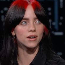 A woman with black and red hair looks surprised.