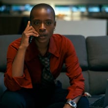 A woman dressed in fashionable business clothes sits on a couch on the phone, looking worried.