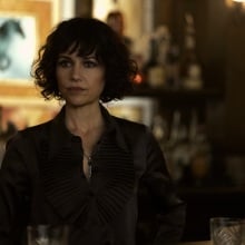 A woman in a black blouse stands behind a bar.