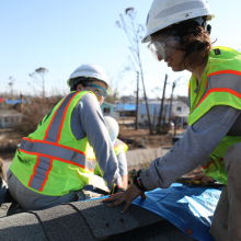 Two people in hard hats and high-visibility vests work on a roof.