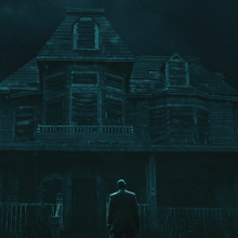 A man stands in front of a tall, dilapidated house at night.