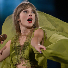 Taylor Swift performs onstage in her Eras Tour, wearing a green floaty dress.
