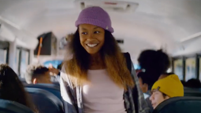 A girl standing in the aisle of a school bus smiling.