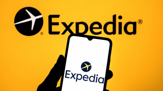 Expedia logo on a smartphone against the backdrop of the Expedia logo on a large screen