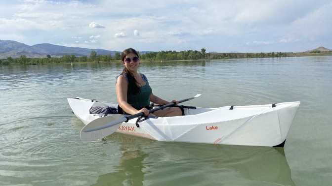 Person with long hair wearing a green top in a white oru kayak on a lake