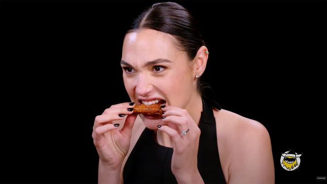 A woman bits into a chicken wing.