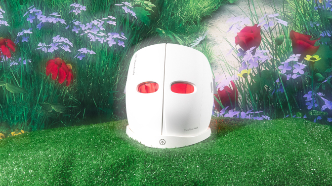 white mask with red LED light shining through eye holes against grass and flower background