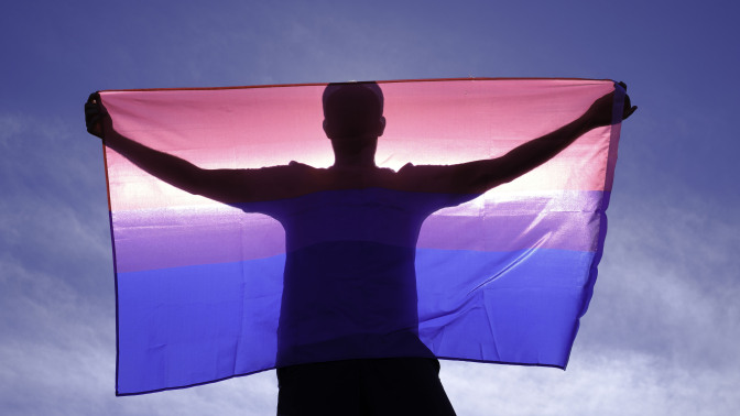 adult man on his back with bisexual flag on a sunny day