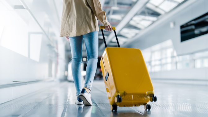 A woman in denim jeans rolling a bright yellow suitcase through an airport. 