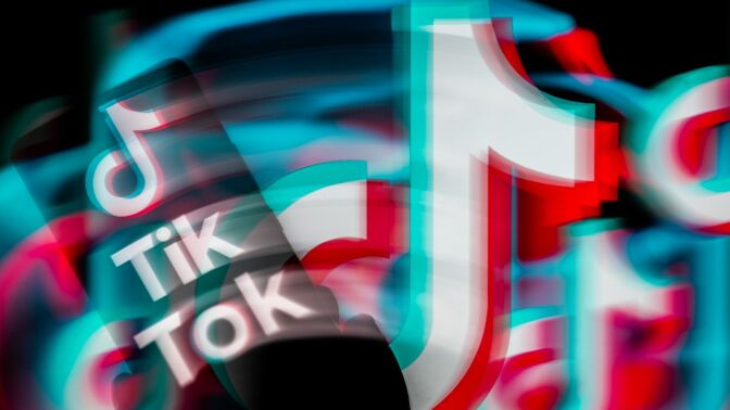 TikTok displayed on a smartphone, blurred, with TikTok icon seen in the background.