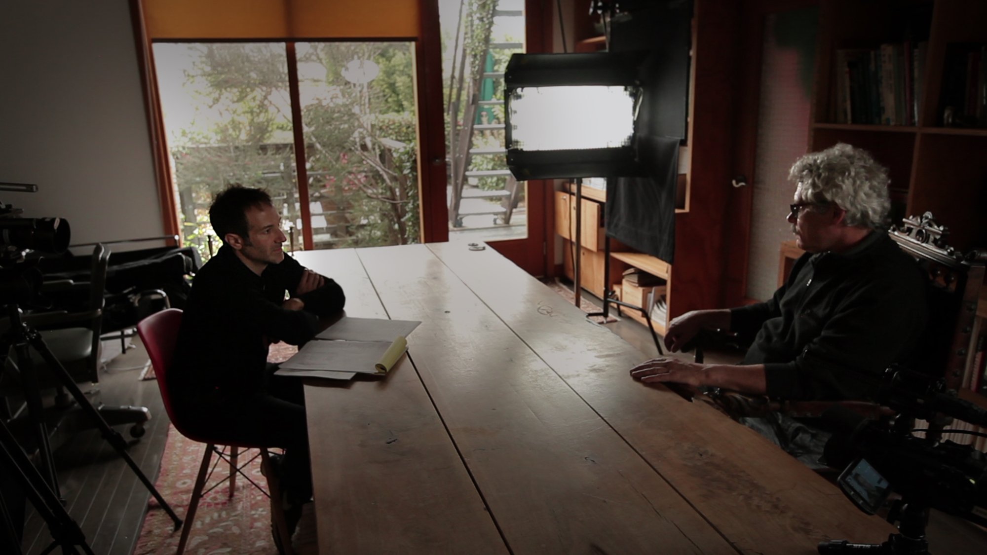A still from the documentary "Icarus" showing two people sitting across from each other at a table doing an interview.
