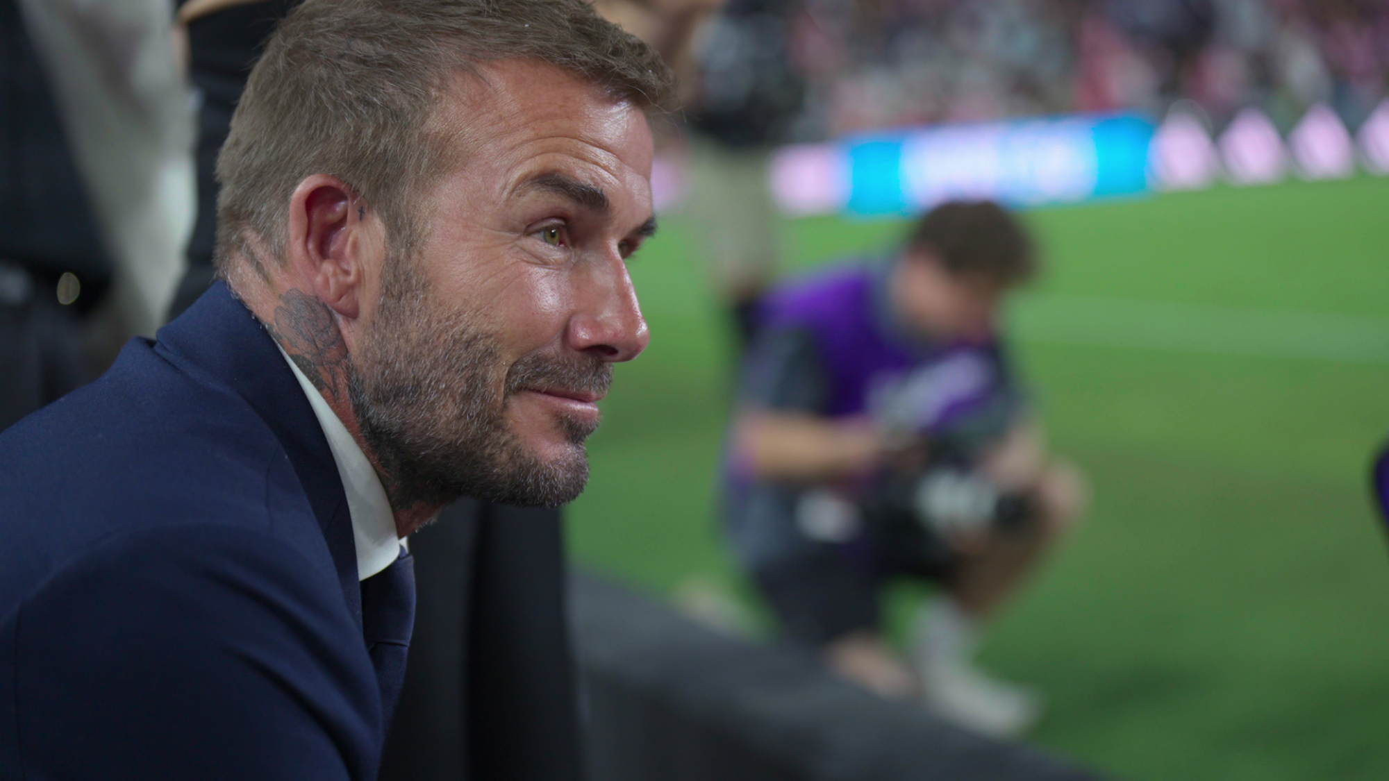 David Beckham sits on the sidelines of a football match.