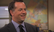 A man (David Costabile as the banker on "The Office") standing in an office wearing a suit and smiling.
